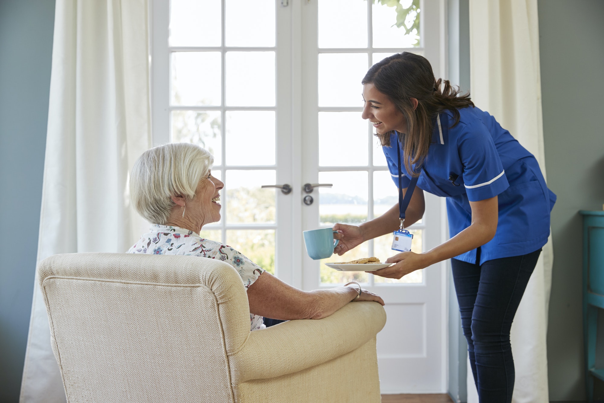 Nurse serving tea and biscuits to senior woman at home